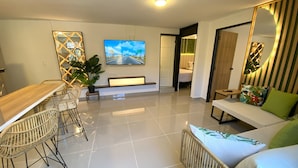 A modern living room with a dining area, a large flat-screen TV, and a sofa with cushions. - Beautiful 2-bedroom apartment in Medellín with Free WiFi, AC- Near El Poblado (Medellín)
