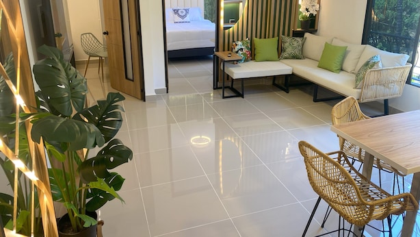 A modern hotel room with a large bed, a sofa, a dining table, and wicker chairs. There is a potted plant and a mirror on the wall. - Beautiful 2-bedroom apartment in Medellín with Free WiFi, AC- Near El Poblado (Medellín)