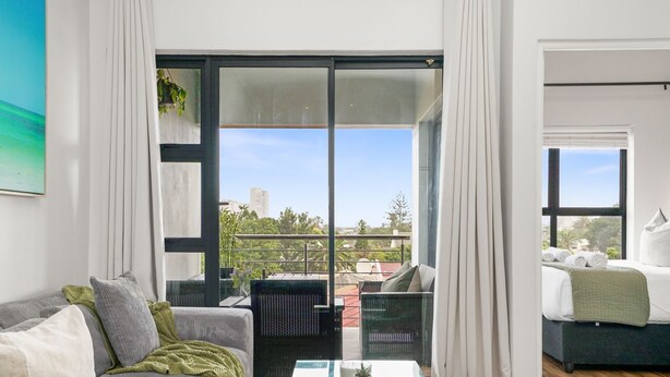 A modern living room with a sofa, a coffee table, and a view of the outdoors through large windows.