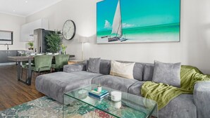 A modern living room with a grey sofa, a glass coffee table, and a painting of a sailboat on the beach.