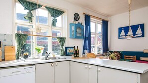 A kitchen with white cabinets, a Siemens dishwasher, a window with curtains, a clock, and a sailboat painting. - Captain House BnB in Fano (Fano)