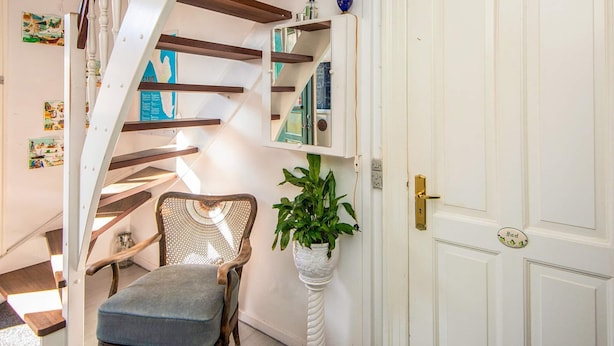 A staircase with wooden beams, a chair, a potted plant, and a white door with a brass handle. - Captain House BnB in Fano (Fano)