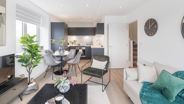 Una sala de estar moderna con un sofá, una mesa de centro y un comedor con sillas. Se ve una cocina al fondo.