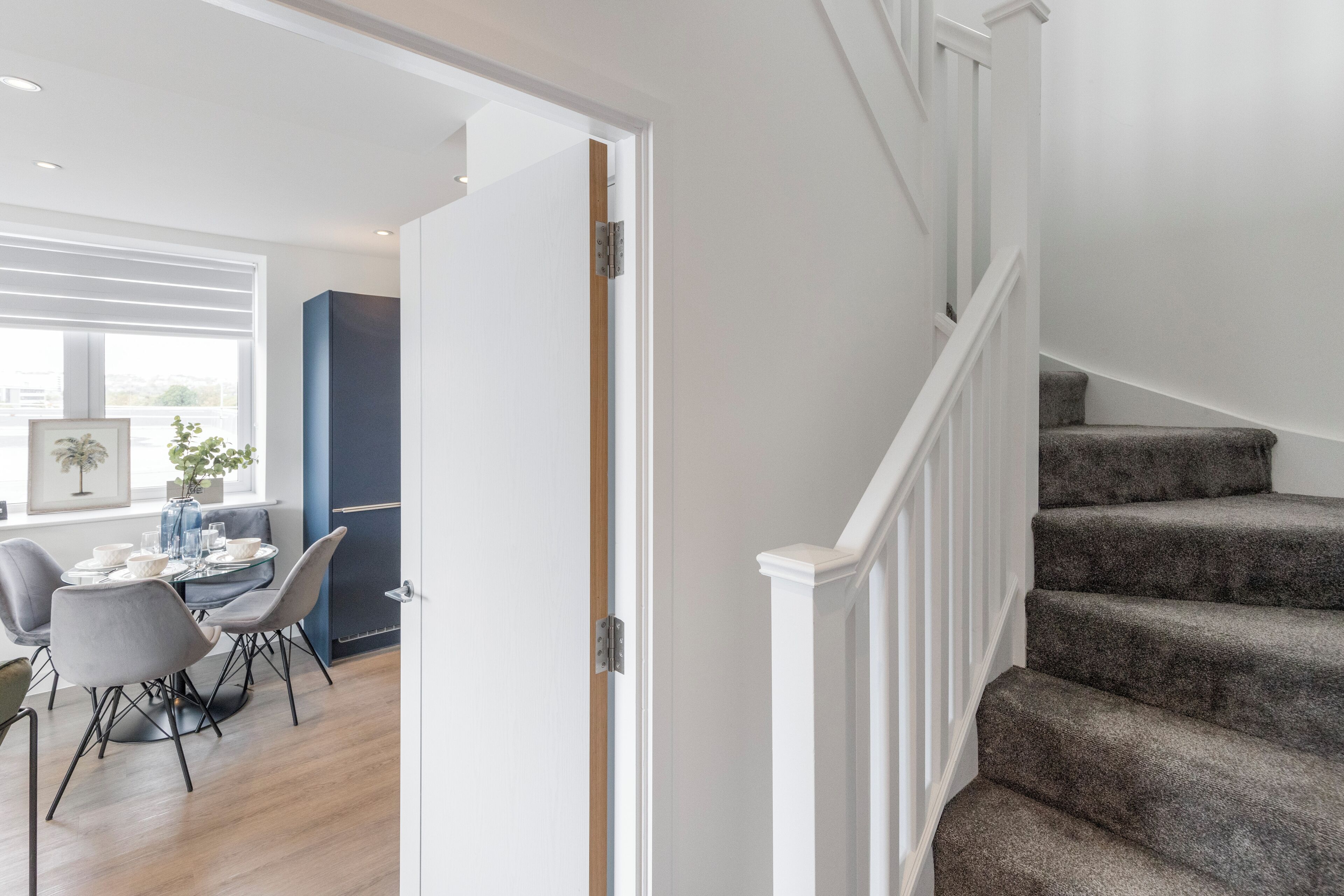 A modern interior with a staircase, a dining area with a round table, and a view of the outdoors.