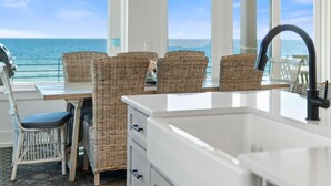 Een keuken met rieten stoelen, een witte spoelbak en uitzicht op de oceaan.