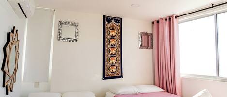 Un dormitorio con dos camas, un ventanal con cortinas rosadas y un aire acondicionado de pared.