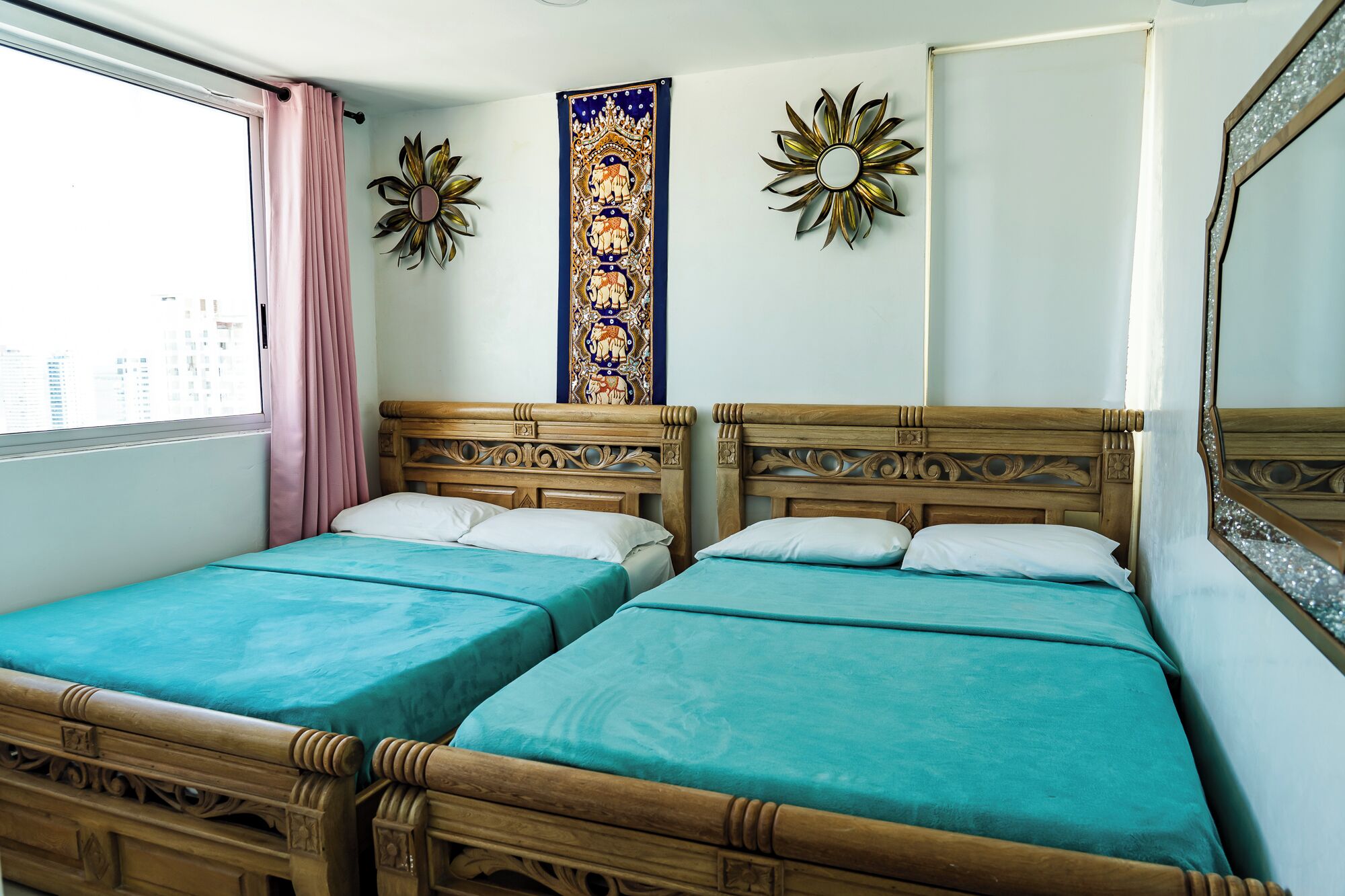 A room with two wooden beds with teal bedding, a large mirror, and decorative wall art.