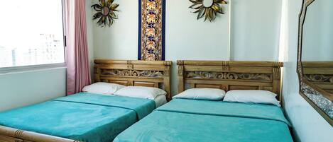 A room with two wooden beds with teal bedding, a large mirror, and decorative wall art.