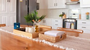 Una cucina con mobili bianchi, un frigorifero in acciaio inossidabile, un fornello e un tavolo da pranzo con un sottopiattino.