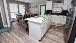 Une cuisine moderne avec des meubles blancs, un îlot en marbre et un coin repas doté de chaises en bois.