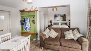 A cozy living room with a brown sofa, white table, and green shelving unit with hanging bags. - Moments From Beach/lodge/naturereserve/ Sandilands (Mablethorpe)