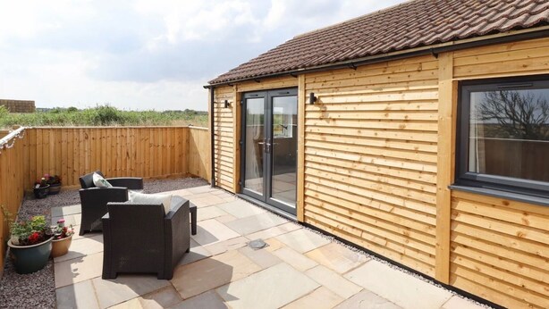 A wooden building with a tiled roof, a sliding glass door, and a patio area with outdoor furniture. - Moments From Beach/lodge/naturereserve/ Sandilands (Mablethorpe)