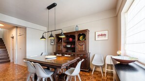 Un comedor con una mesa de madera, sillas blancas, un aparador de madera oscura y lámparas colgantes.