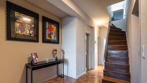 Un pasillo con suelo de madera, una escalera y dos cuadros en la pared.