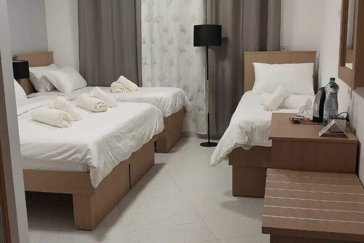 A hotel room with two single beds, a bedside table with a lamp, a small table with a bottle and a notebook, and a mirror on the wall.