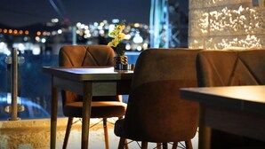 A restaurant with a table and chairs, a vase with flowers, and a city view in the background. - St Barbara Hotel (Bethlehem)