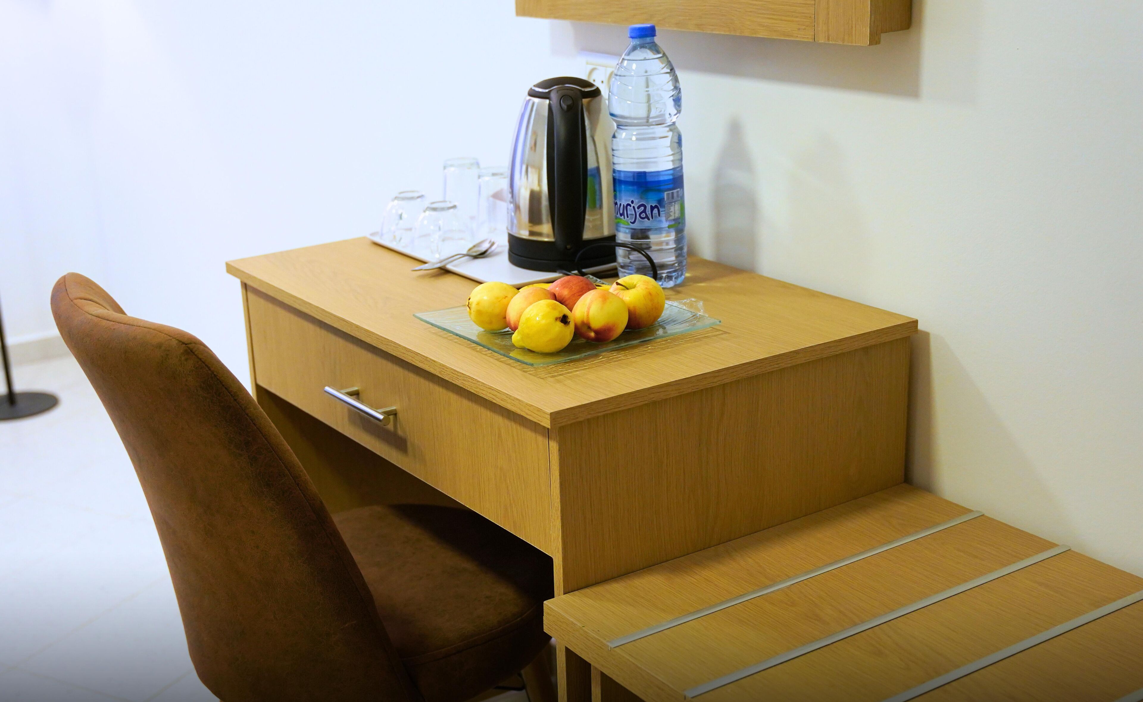 Ein Holztisch mit einem Glaseinsatz, der Früchte, eine Wasserflasche und einen Wasserkocher enthält.