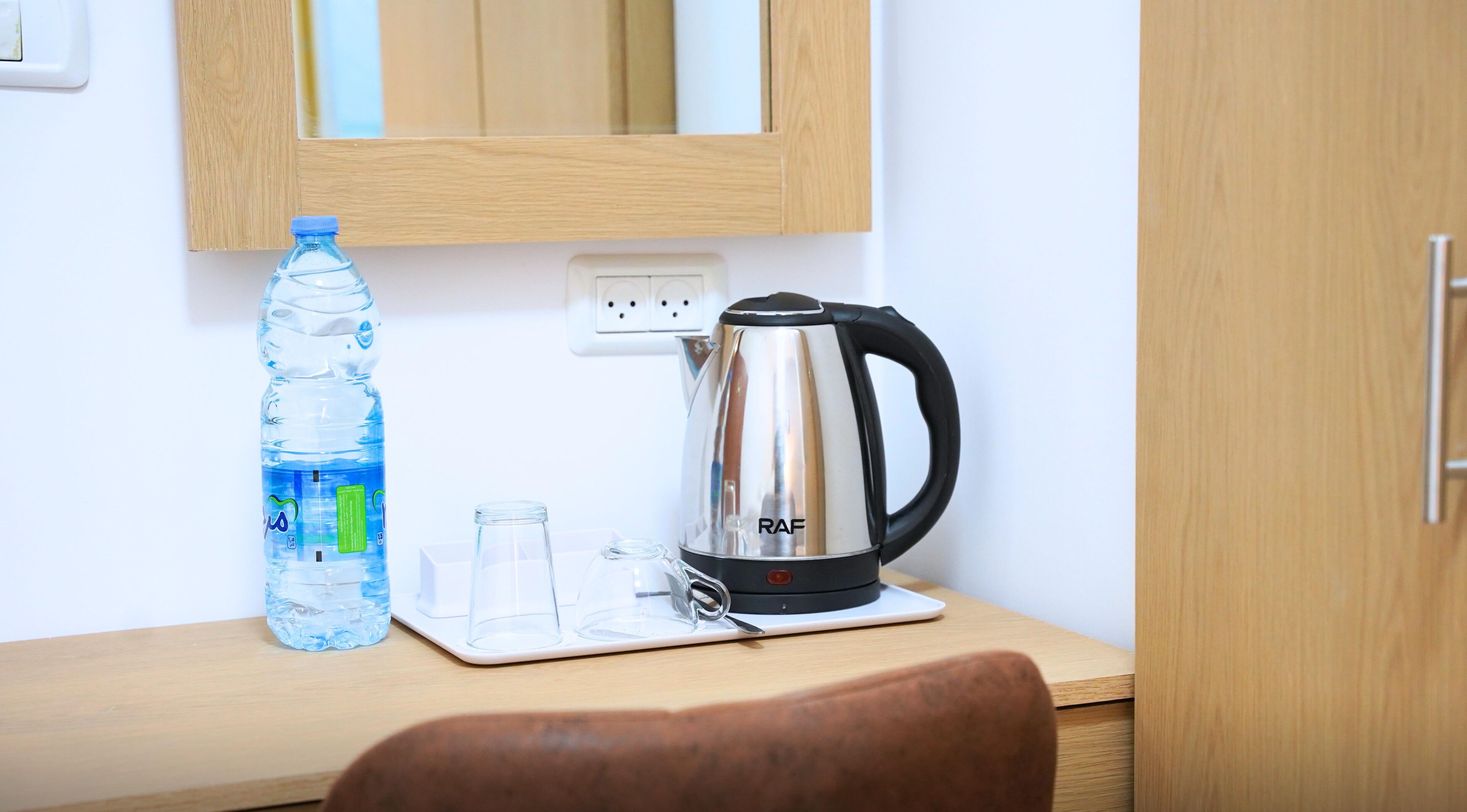 A wooden table with a water bottle, a glass, and a kettle.