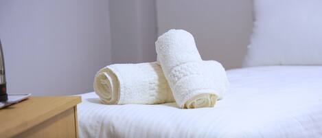 A neatly made bed with white linens and two rolled white towels on the side.