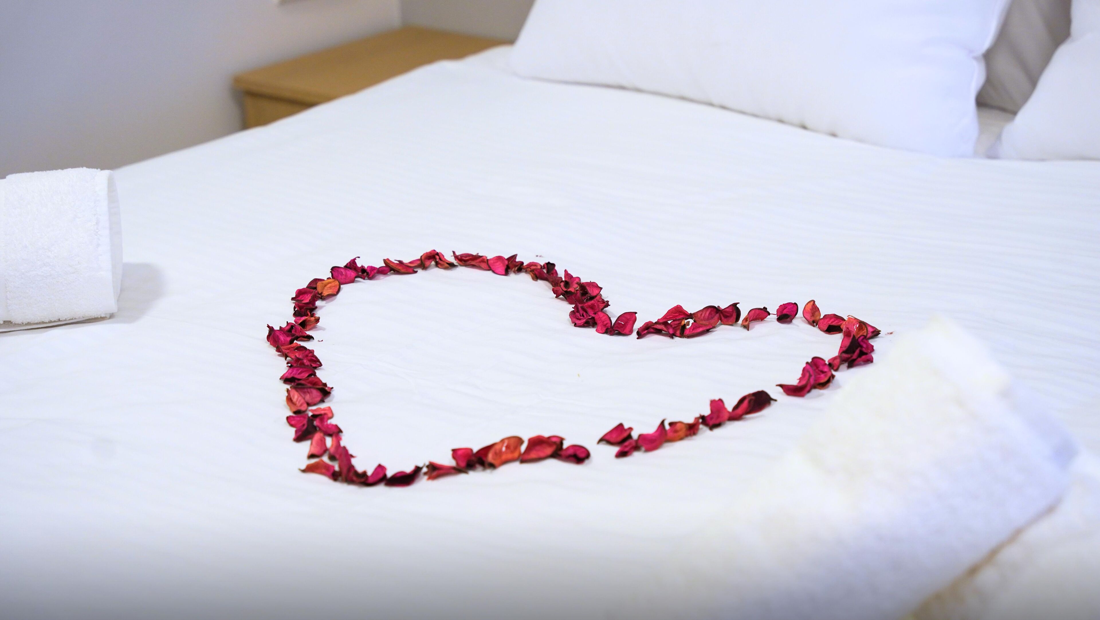 A neatly made bed with a heart-shaped decoration of dried rose petals.
