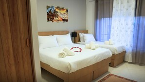 A double room with two beds, white bedding, a wooden headboard, a small bedside table with a lamp, and a tropical artwork on the wall. - St Barbara Hotel (Bethlehem)