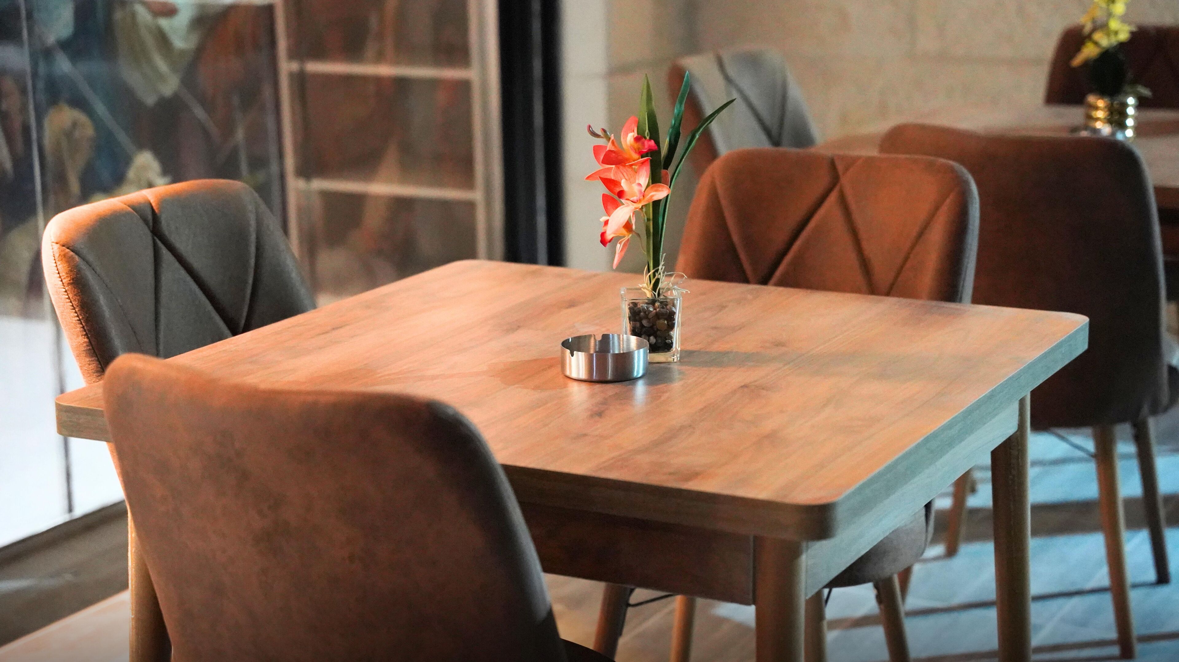 A wooden dining table with four chairs, a metal ashtray, and a small vase with flowers.