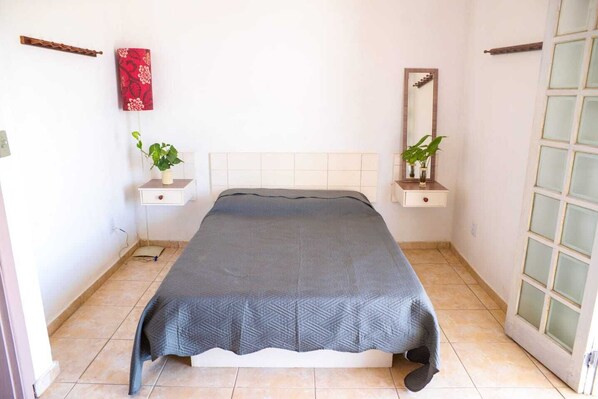 A bedroom with a bed, two bedside tables, a mirror, and a window.