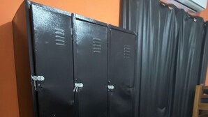 Un conjunto de taquillas negras frente a una pared naranja, con una silla de madera y una cortina al fondo.