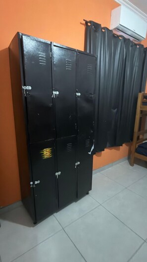 Une rangée de casiers noirs adossés à un mur orange, avec une chaise en bois et un rideau en arrière-plan.