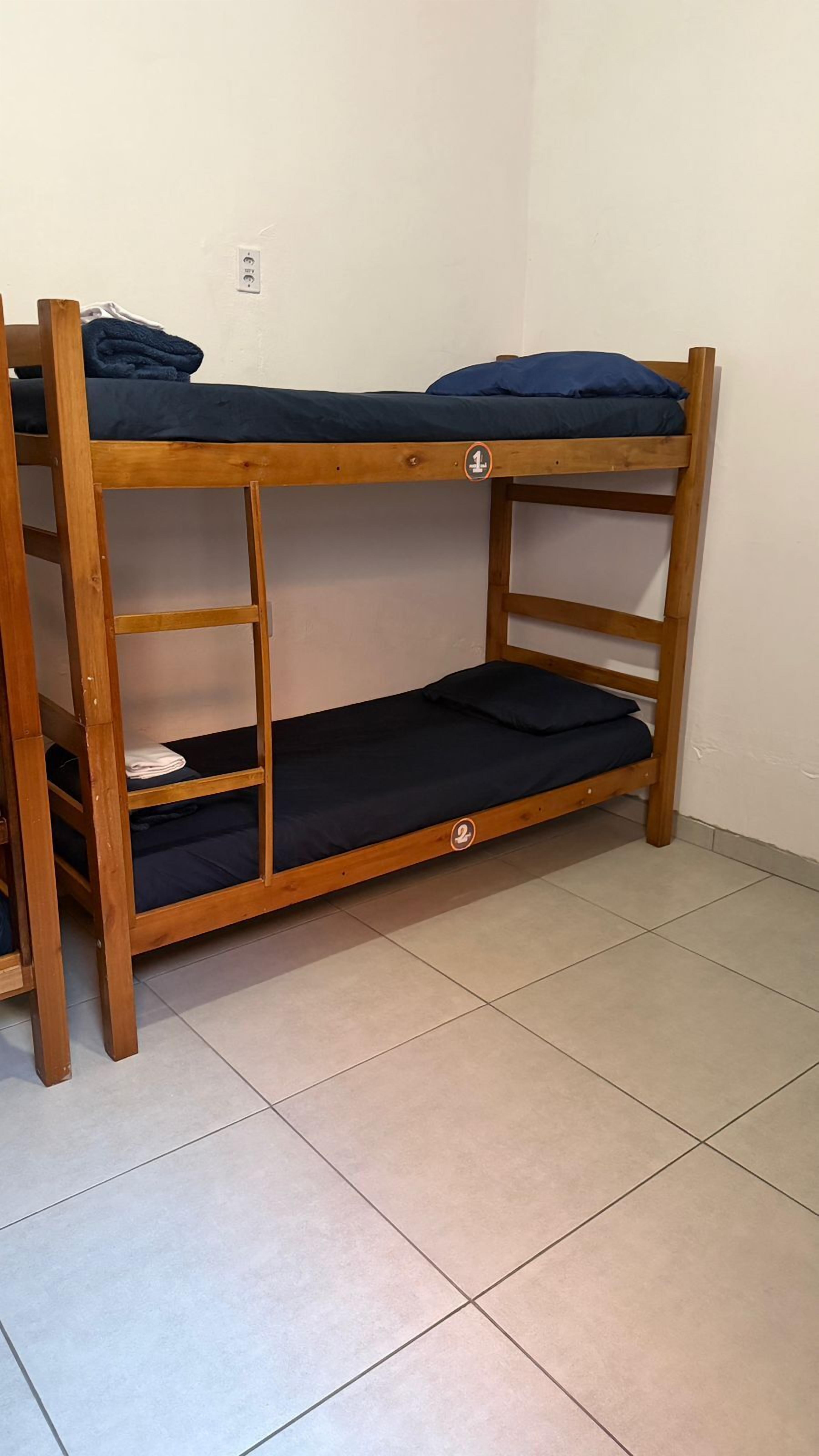 A bunk bed with two levels, a wooden frame, and a tiled floor.