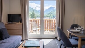 A room with a sofa, a table with a board game, a dining table set for two, and a balcony with a view of mountains. - Wifi, resort center, fitness, balcony, tv, 42m², Brides Les Bains (Brides-les-Bains)