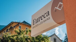A sign for "Eureka BRIDES-LES-BAINS" with a view of buildings and trees in the background.