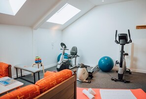A room with a bed, exercise equipment, a small table, and a window.
