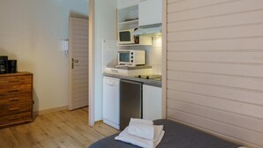 Een compacte keuken met een magnetron, broodrooster en vaatwasser. Ook zichtbaar is een houten dressoir en een bed met een opgevouwen handdoek.