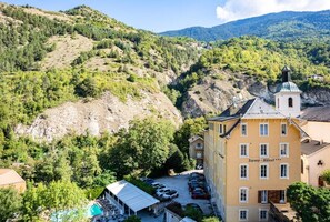 Et hotel med swimmingpool, omgivet af frodigt grønt og bakker.