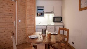 Cocina compacta con armarios blancos, microondas y una pequeña ventana. Una mesa de madera con sillas está dispuesta para dos.