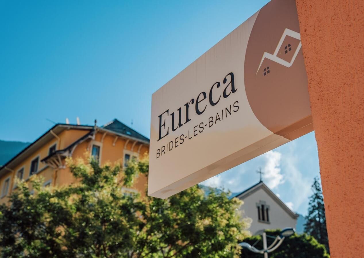 A sign for "Eureka BRIDES-LES-BAINS" with a view of buildings and trees in the background.