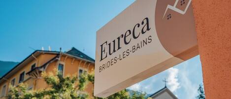 A sign for "Eureka BRIDES-LES-BAINS" with a view of buildings and trees in the background.