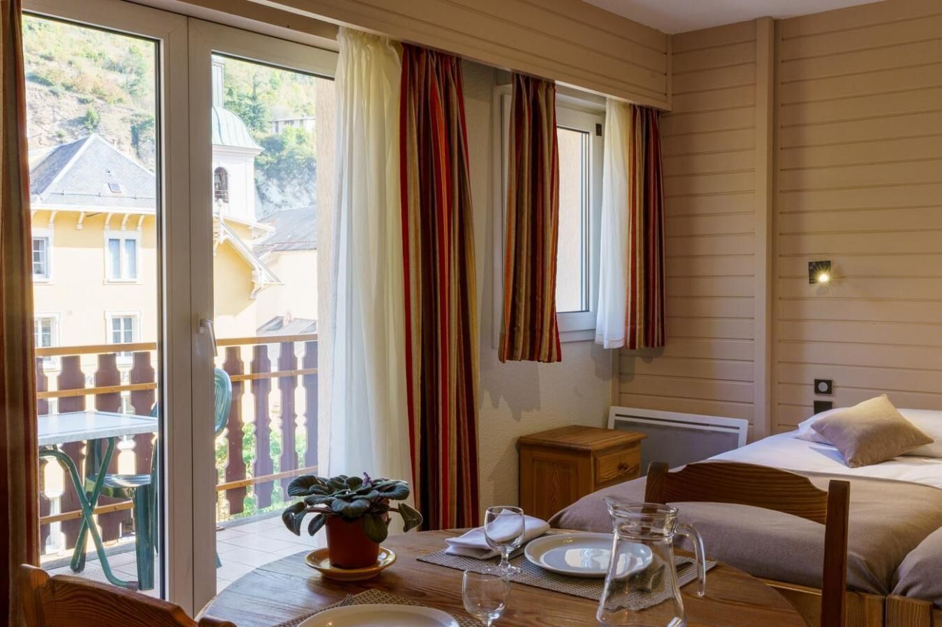 Una habitación con una cama, una mesa con una planta y vistas a un balcón con barandilla.