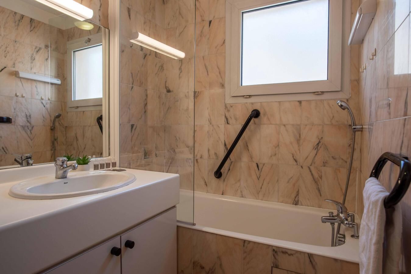 Een moderne badkamer met een marmeren wand, een grote spiegel, een badkuip en een handgreep.