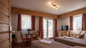A hotel room with two beds, a small table with chairs, a TV, and a balcony with curtains. - Wifi, 200m from ski lifts, fitness, balcony, tv, 31m², Brides Les Bains (Brides-les-Bains)