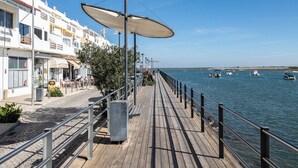 A wooden boardwalk with metal railings, leading to a waterfront with boats.