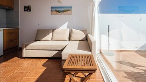 A modern living room with a sofa, a small wooden table, and a view of the sky through a large window.