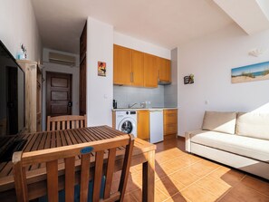 Um espaço compacto com mesa de jantar, cadeiras de madeira, sofá, área de cozinha com armários de madeira, máquina de lavar e uma pia pequena.
