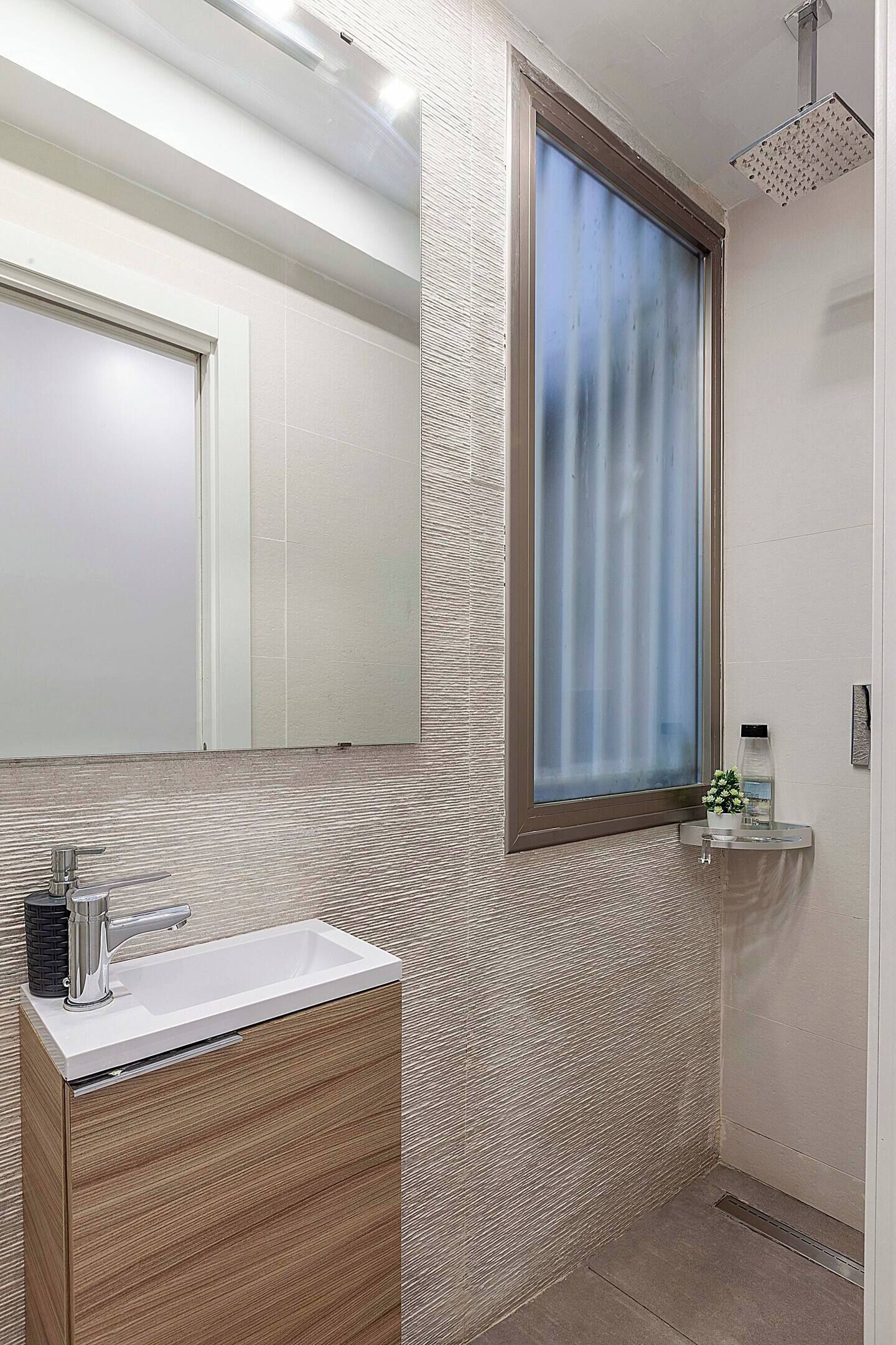 Une salle de bain moderne avec un grand miroir, un lavabo et un espace douche.