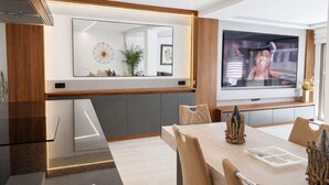Une cuisine moderne avec un grand miroir, un coin repas comprenant une table et des chaises, et un téléviseur fixé au mur.