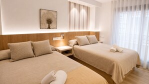 Une chambre d’hôtel avec deux lits, une table de chevet, une lampe fixée au mur et une fenêtre avec des rideaux légers.