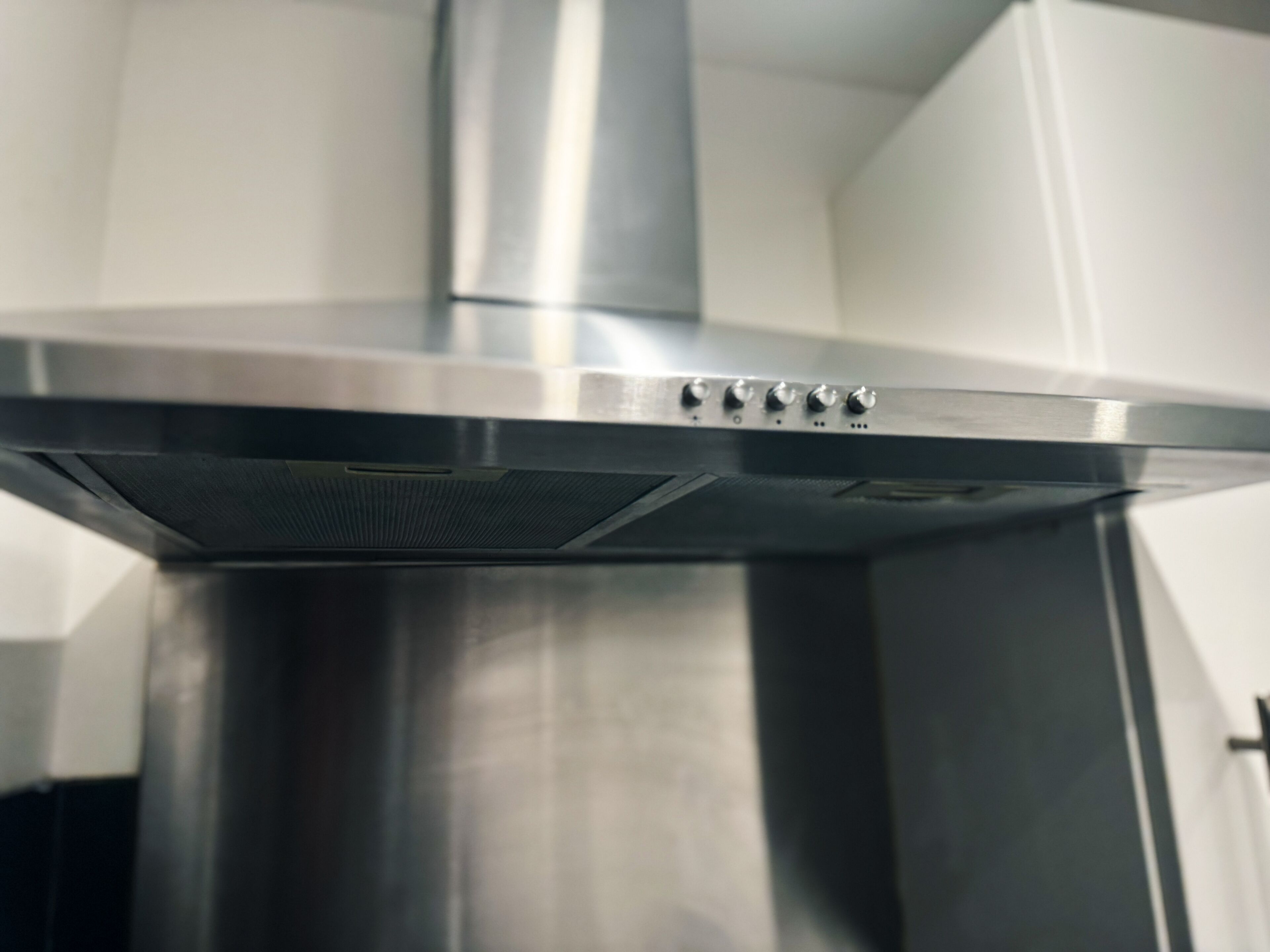 A stainless steel kitchen hood with control knobs.