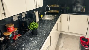 Une cuisine moderne avec des meubles blancs, un plan de travail en granit noir, un évier en acier inoxydable, un four à micro-ondes et un grille-pain.