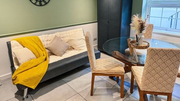 Un salon comprenant un canapé, des fauteuils, une table en verre, une horloge et une fenêtre donnant sur un beau paysage.